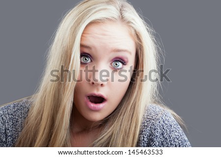 portrait of a pretty caucasian girl with blond hair looking shocked with her mouth popped open and eyes wide