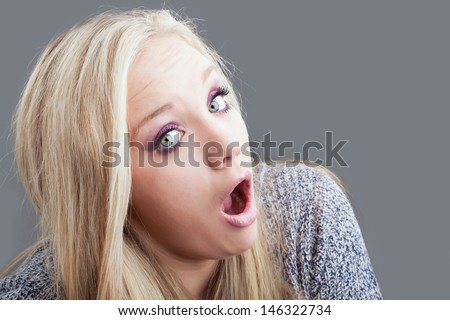 portrait of a caucasian girl with blond hair in shock with her head tilted to the side on a gray background