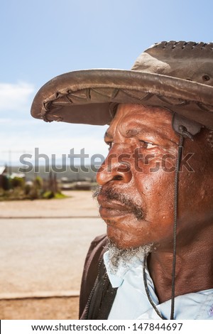 cropped portrait of an old african man outside looking to the side in interest wearing a farmers hat