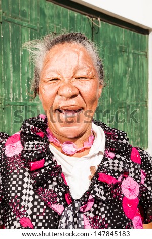 portrait of an african homeless woman smiling open mouthed showing off missing teeth in front of a green wooden door