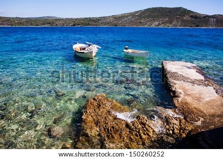 two small boats docked on an old dock floating in the shallow clear water