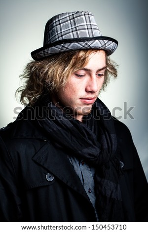 portrait of a handsome caucasian man wearing a warm black scarf and gray check hat looking down in thought