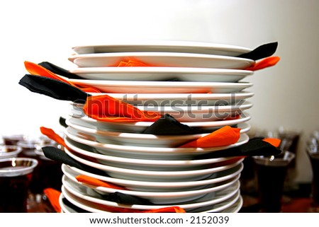 Plates stacked ontop of each other with orange and black napkins