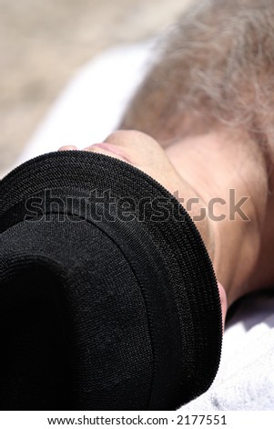 Man sunbathing on the beach with black fedora hat