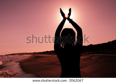 Silhouette of a woman on the beach holding the sun between her fingers
