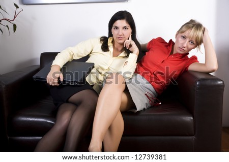 Two attractive businesswoman sitting very close to each other on a office sofa.