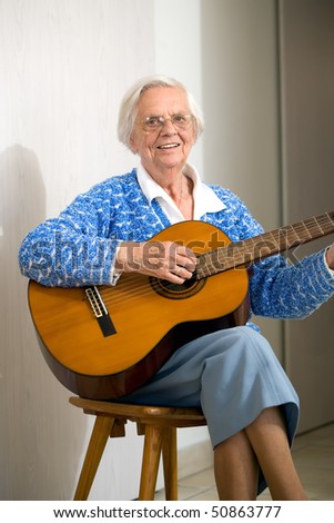 Elderly woman playing the guitar wearing a blue knitted top.