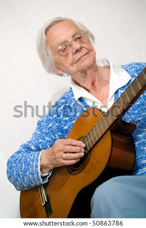 Elderly woman playing the guitar wearing a blue knitted top.