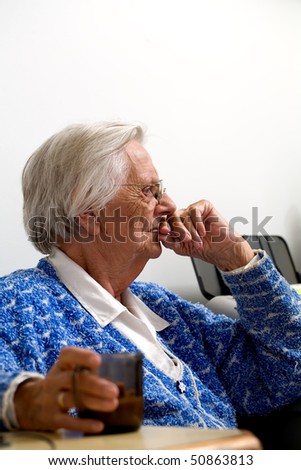 Elderly woman witting with a coffee in one hand and her other hand over her lips.