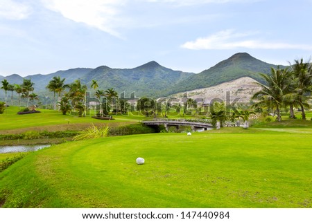 Golf course in luxury resort. Golf green field on the background of the mountains and beautiful palm tree over blue sky with white clouds view