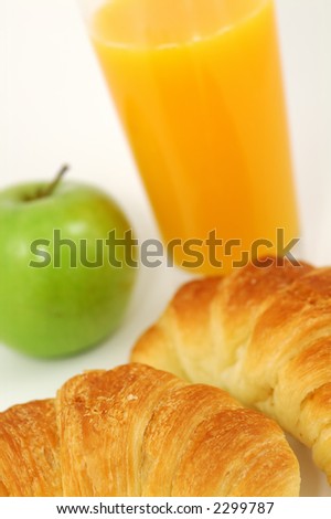 Fresh-baked croissant, orange juice and green apple.  Shallow DOF. Focus on croissant.