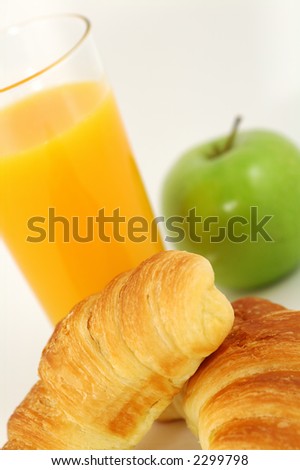 Fresh-baked croissant, orange juice and green apple.  Shallow DOF. Focus on croissant.