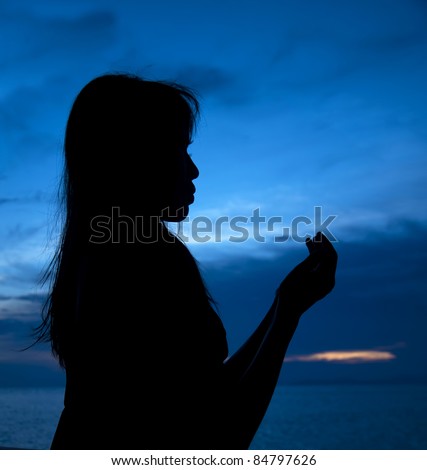 Silhouette of woman which sits near sea opposite sun and laid down hands before itself and prays
