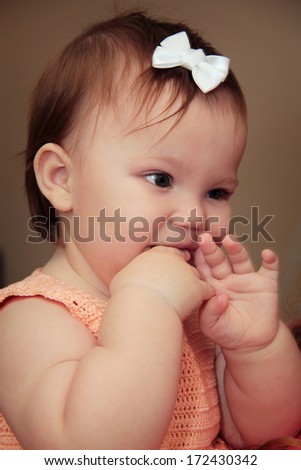 Cute little baby girl with hands by mouth and with bow in hair