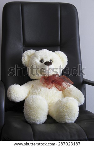 Teddy bear with bow sitting on black chair