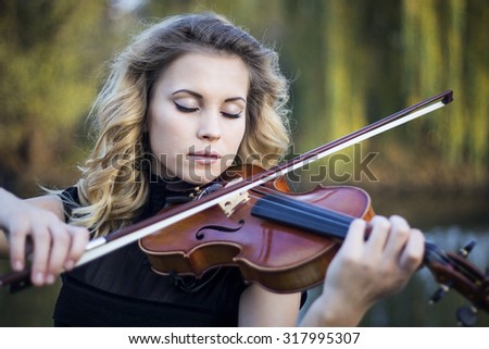 Young woman playing the violin at park. Shallow depth of field.
