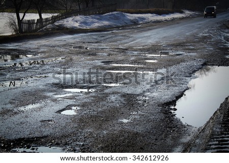 Road destroyed after winter in Ukraine. Puddles in the pits in the road.