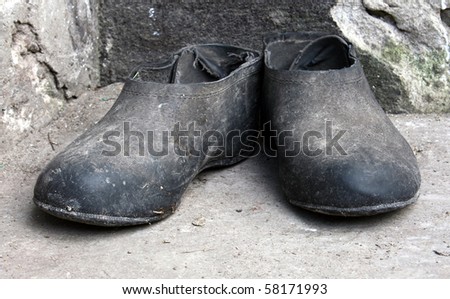 Old dirty galoshes standing on the concrete floor near the wall