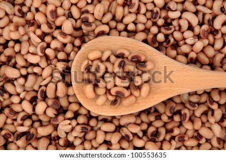 Cooked black eyed peas on a wooden cooking spoon and forming a background.