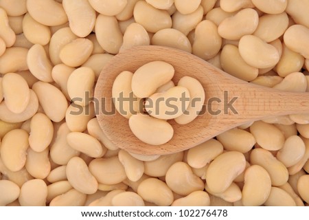 Butter beans in a wooden cooking spoon and forming a textured background.