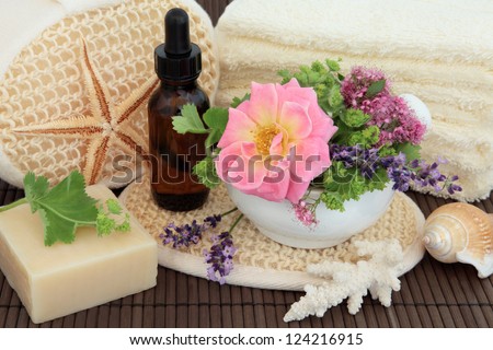 Spa arrangement of herb and flower leaf sprigs, cream towels, exfoliating  scrub, aromatherapy essential oil bottle, sea coral and natural soap over bamboo.