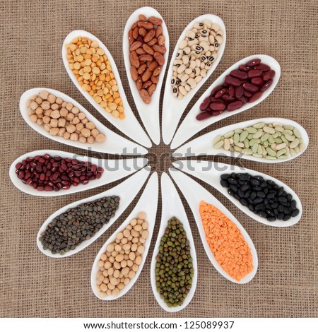 Pulses vegetable selection of peas, beans and lentils in white porcelain bowls over hessian background.