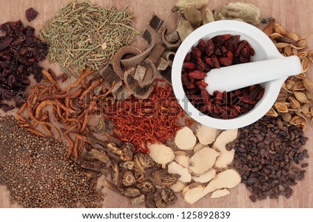 Traditional chinese herbal medicine selection with mortar and pestle over papyrus background.