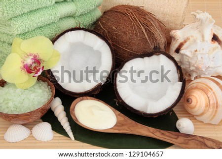 Coconut spa products with body moisturiser, green bath salts, exfoliating scrub, towels and sea shells over bamboo and leaf background.