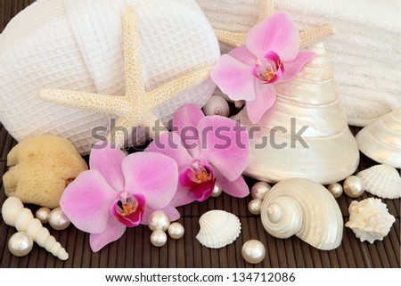 Orchid flower arrangement with spa and bathroom accessories and mother of pearl shells over bamboo background.