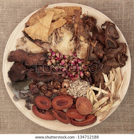 Traditional chinese herbal medicine selection on a round wooden bowl over hessian background.