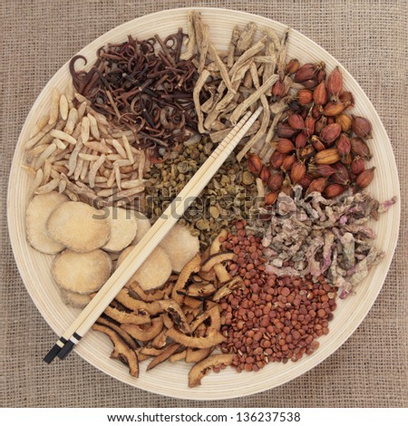 Traditional chinese herbal medicine selection on a round wooden bowl with chopsticks over hessian background.