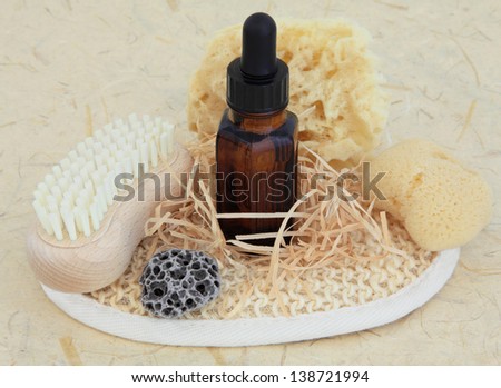Aromatherapy essential oil bottle, natural sponges, pumice, nail brush and exfoliating scrub over mottled cream background.