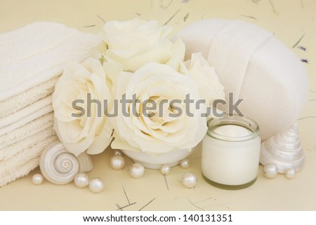 Rose flowers with bathroom accessories of moisturiser cream, pearls and shells over mottled background.