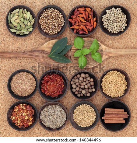 Spice, herb and food ingredient sampler in wooden spoons and bowls over cork background.
