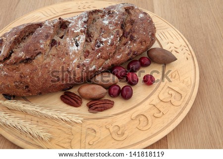 Pecan and cranberry homemade brown bread on a beech wood bread board over oak background.