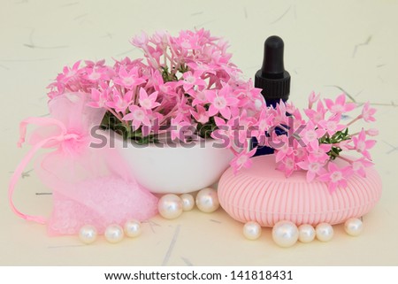 Verbena flowers with aromatherapy essential oil bottle, pink soap, bath crystals and pearls over mottled cream background.