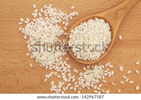 Risotto arborio white rice in a beech wood spoon over wooden board.