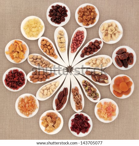 Large dried fruit and nut selection in white porcelain bowls over hessian background.