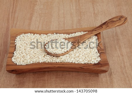 Risotto arborio short grain rice in an olive wood bowl with spoon over papyrus background.