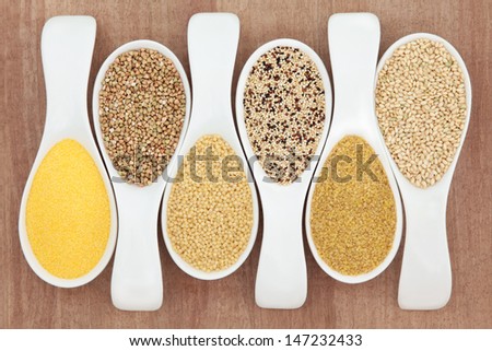 Healthy grain food selection in white porcelain spoons over papyrus background. Polenta, buckwheat, couscous, quinoa, bulghur wheat and sweet rice, left to right.