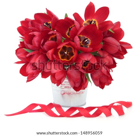 Red tulip flower arrangement in a metal vase with ribbons over white background.