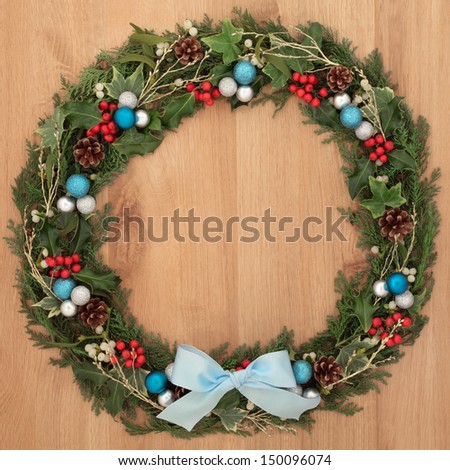 Christmas floral wreath decoration with blue and silver baubles, bow, holly and winter greenery over oak background.