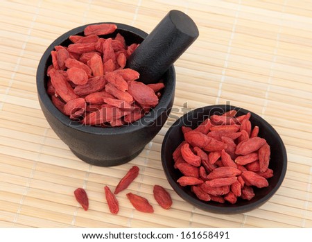 Wolfberry fruit used in chinese herbal medicine in a mortar with pestle and bowl over bamboo. Gou qi zi.