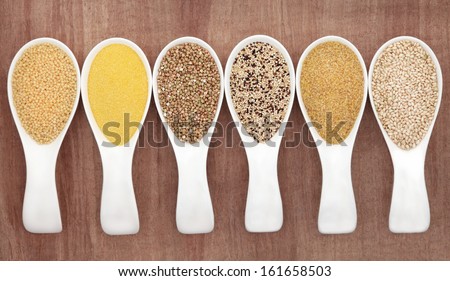 Grain food selection in white china porcelain spoons over papyrus background.