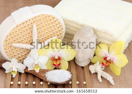 Spa and bathroom setting with buddha, orchid flowers, sea salt,  shells, towels and exfoliating scrub.