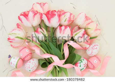 Tulip flower arrangement with easter eggs and ribbon curl over handmade paper background.