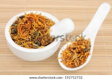 Dried calendula flowers used in chinese herbal medicine in a porcelain mortar with pestle and spoon.