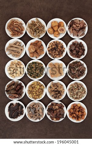 Large chinese herbal medicine selection in white china bowls over lokta paper background.