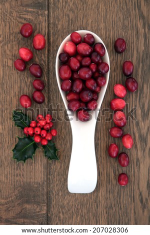 Christmas cranberry fruit in a porcelain scoop with holly over oak background.