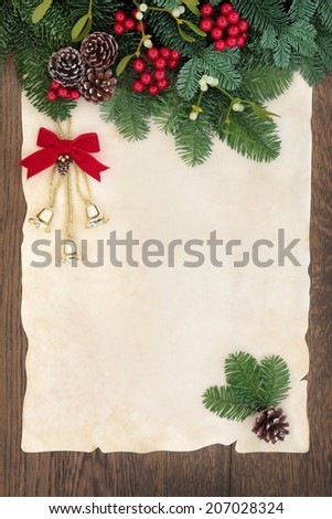 Christmas and winter background border with bells, fir, red berry sprays, mistletoe and pine cones over old parchment paper and oak wood.